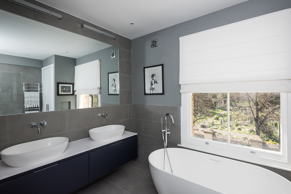 Inspiration for a large modern family bathroom in London with blue cabinets, a freestanding bath, a shower/bath combination, a wall mounted toilet, grey tiles, ceramic tiles, green walls and ceramic flooring.