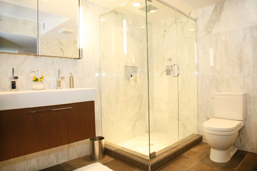 Mid-sized minimalist master brown tile and stone tile marble floor corner shower photo in Miami with a wall-mount sink, flat-panel cabinets, medium tone wood cabinets, a two-piece toilet and beige walls