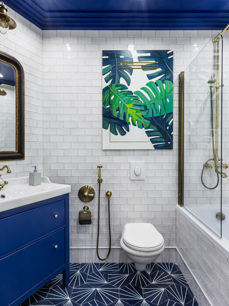 Bild på ett vintage badrum, med blå skåp, en vägghängd toalettstol, vit kakel, tunnelbanekakel, cementgolv, ett konsol handfat, blått golv, med dusch som är öppen och släta luckor
