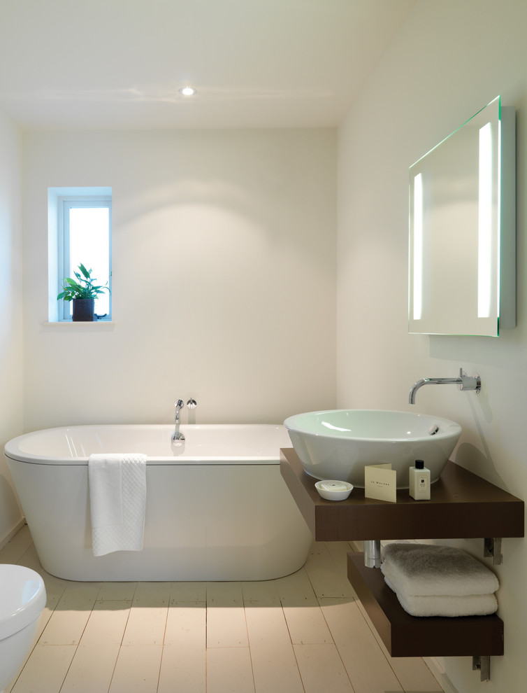 Inredning av ett modernt en-suite badrum, med skåp i mörkt trä, ett fristående badkar, vita väggar, ljust trägolv och ett fristående handfat