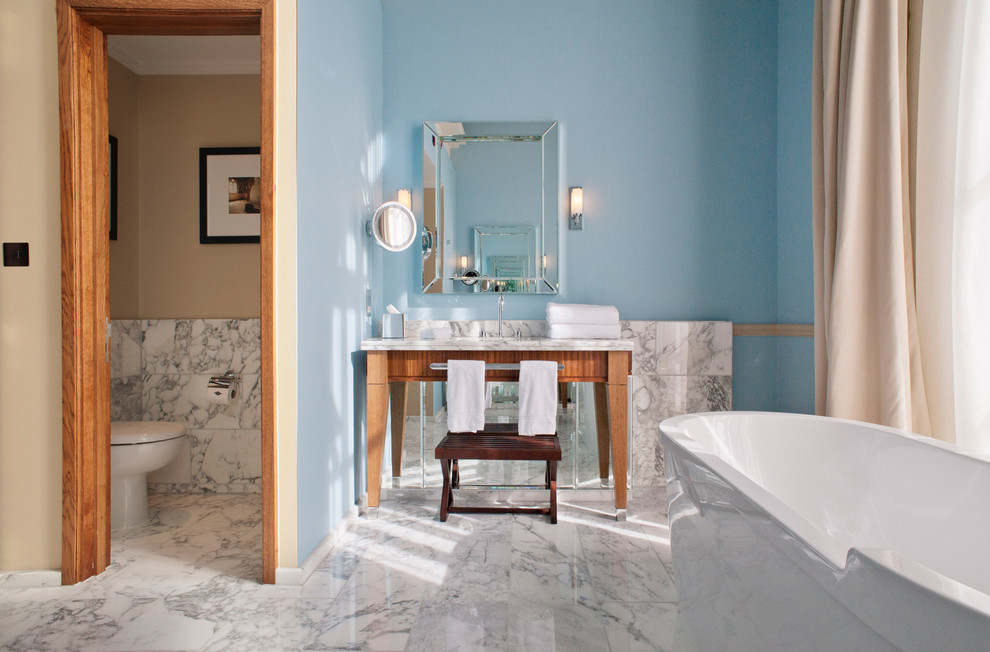 Immagine di una stanza da bagno chic con vasca freestanding, lastra di pietra, pareti blu, pavimento in marmo e lavabo a consolle