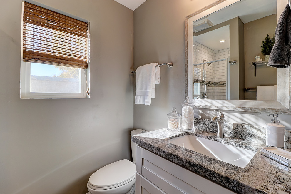 Example of a small transitional master white tile and subway tile laminate floor and brown floor alcove shower design in Phoenix with shaker cabinets, white cabinets, a one-piece toilet, gray walls, an undermount sink, granite countertops, a hinged shower door and gray countertops