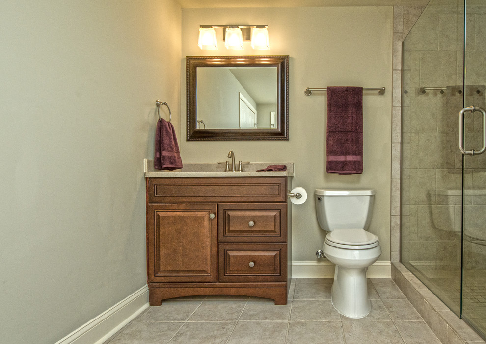 Cette image montre une grande salle de bain traditionnelle en bois brun avec un mur beige, un sol en carrelage de céramique, un placard avec porte à panneau surélevé, WC séparés, un carrelage beige, des dalles de pierre, un lavabo encastré, un plan de toilette en stratifié, un sol beige et une cabine de douche à porte battante.