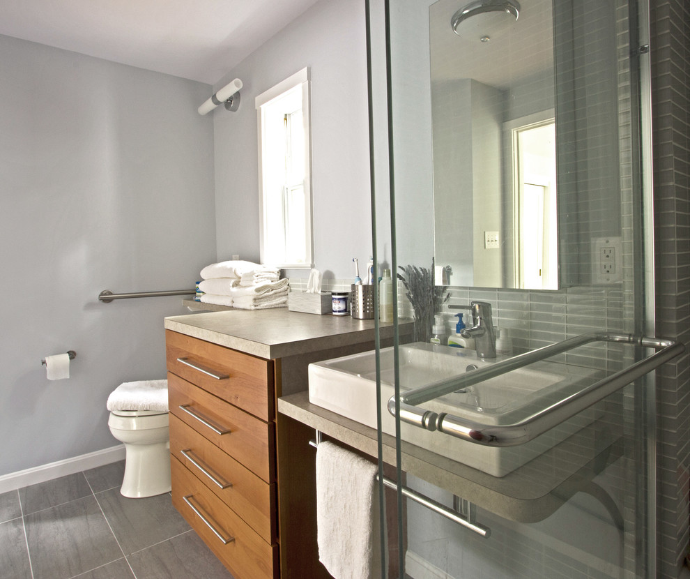 Inredning av ett modernt mellanstort badrum, med ett fristående handfat, släta luckor, laminatbänkskiva, en dusch i en alkov, en toalettstol med hel cisternkåpa, grå kakel, glaskakel, grå väggar, klinkergolv i porslin och skåp i mellenmörkt trä