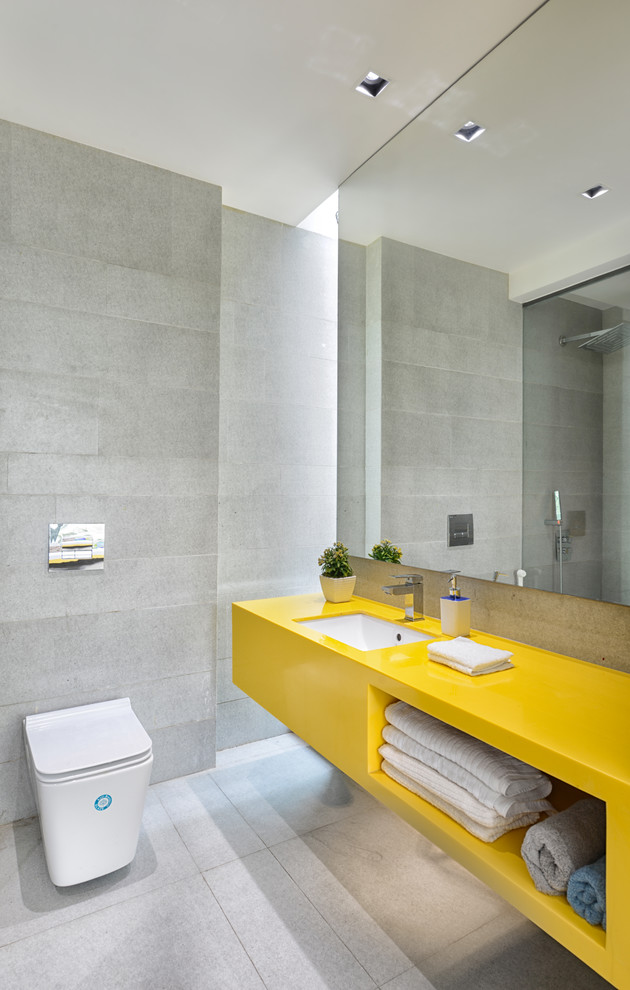 Contemporary grey and yellow ensuite bathroom in Ahmedabad with open cabinets, yellow cabinets, a corner shower, a wall mounted toilet, grey tiles, grey walls, a submerged sink, grey floors and yellow worktops.