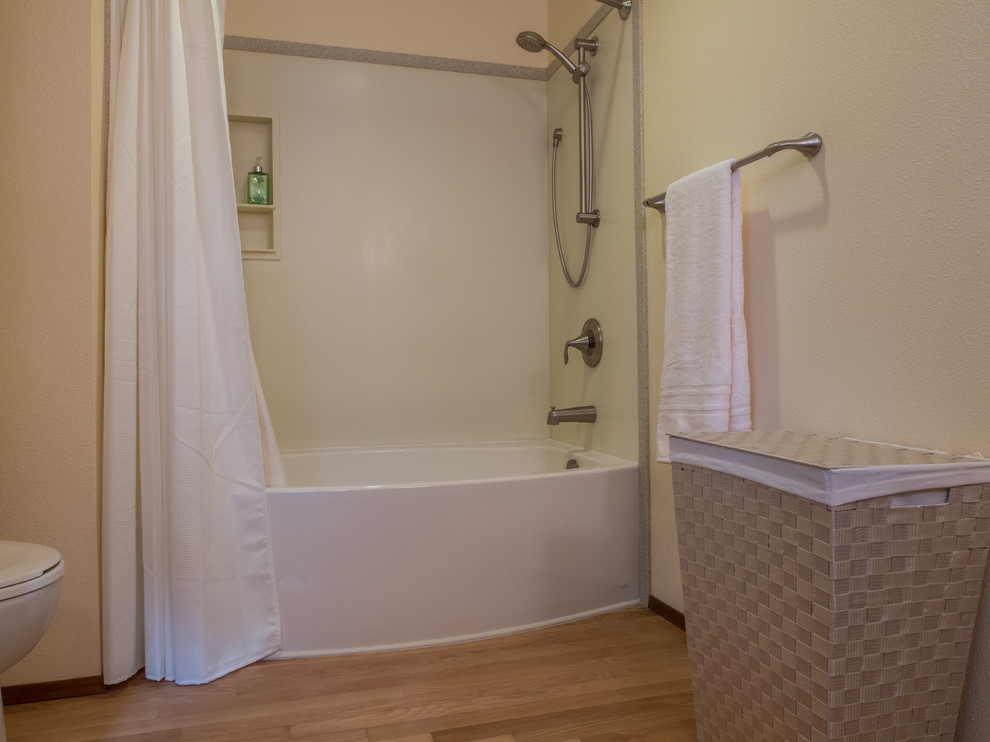 Klassisk inredning av ett mellanstort flerfärgad flerfärgat en-suite badrum, med ett undermonterad handfat, luckor med infälld panel, skåp i mellenmörkt trä, bänkskiva i akrylsten, ett badkar i en alkov, en dusch/badkar-kombination, en toalettstol med separat cisternkåpa, gula väggar, ljust trägolv, brunt golv och dusch med duschdraperi