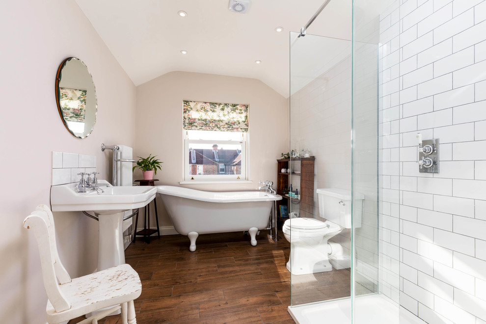 Design ideas for a medium sized classic ensuite bathroom in Hampshire with a claw-foot bath, a walk-in shower, white tiles, pink walls, a pedestal sink, an open shower, brown floors, a two-piece toilet, metro tiles and dark hardwood flooring.