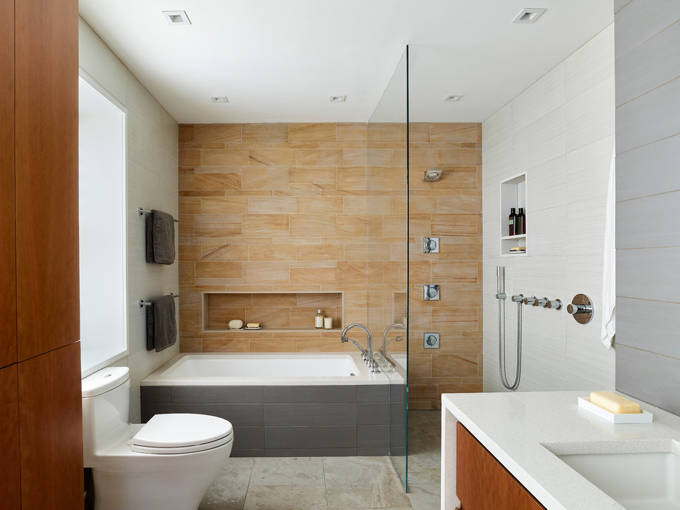 Cette image montre une salle de bain principale minimaliste en bois brun de taille moyenne avec un placard à porte plane, une baignoire encastrée, une douche à l'italienne, WC à poser, un carrelage orange, un carrelage de pierre, un mur gris, un sol en carrelage de porcelaine, un lavabo encastré et un plan de toilette en quartz modifié.