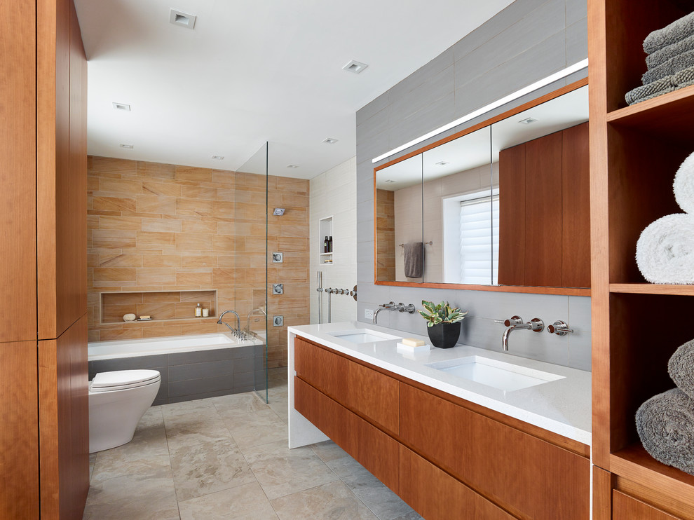 Inspiration for a medium sized modern ensuite bathroom in Philadelphia with flat-panel cabinets, medium wood cabinets, a submerged bath, a built-in shower, a one-piece toilet, stone tiles, grey walls, porcelain flooring, a submerged sink, engineered stone worktops, brown tiles, beige floors and an open shower.