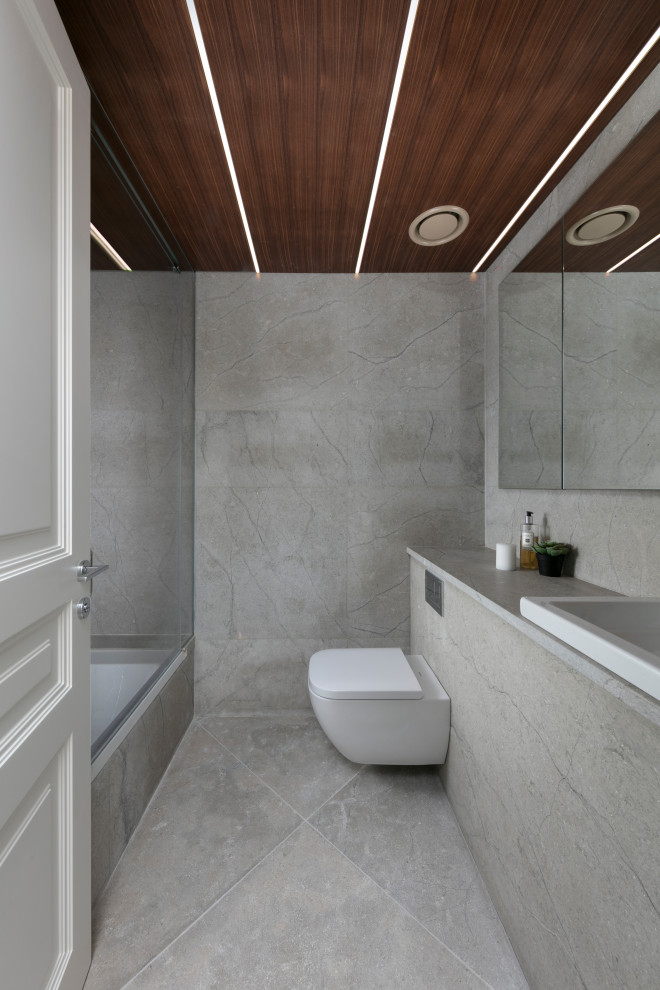Bild på ett mellanstort funkis grå grått badrum för barn, med ett undermonterat badkar, en dusch/badkar-kombination, en vägghängd toalettstol, grå kakel, grå väggar, marmorgolv, ett undermonterad handfat, marmorbänkskiva, grått golv och dusch med skjutdörr