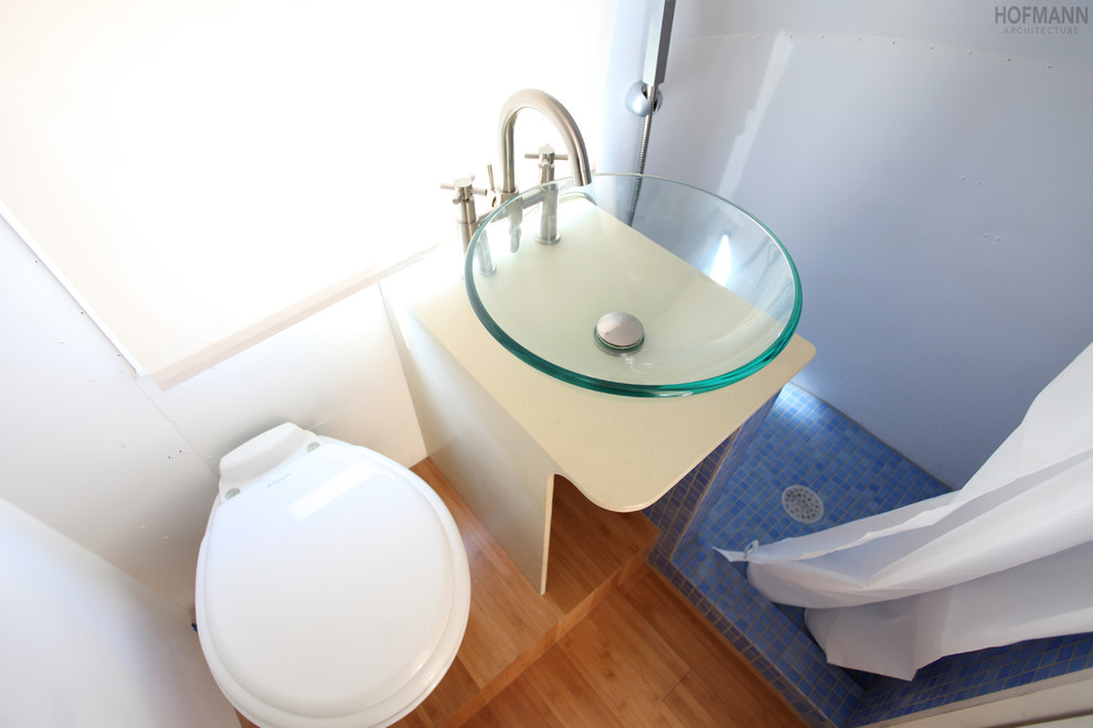 Idéer för små funkis badrum med dusch, med ett fristående handfat, öppna hyllor, beige skåp, bänkskiva i akrylsten, en hörndusch, en toalettstol med hel cisternkåpa, blå kakel, glaskakel, vita väggar och bambugolv