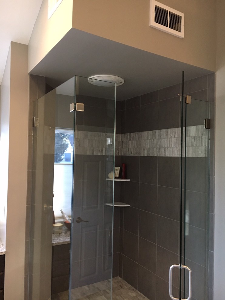 Example of a large transitional master gray tile and stone tile dark wood floor and brown floor bathroom design in San Diego with raised-panel cabinets, black cabinets, a two-piece toilet, gray walls, an undermount sink, granite countertops and a hinged shower door