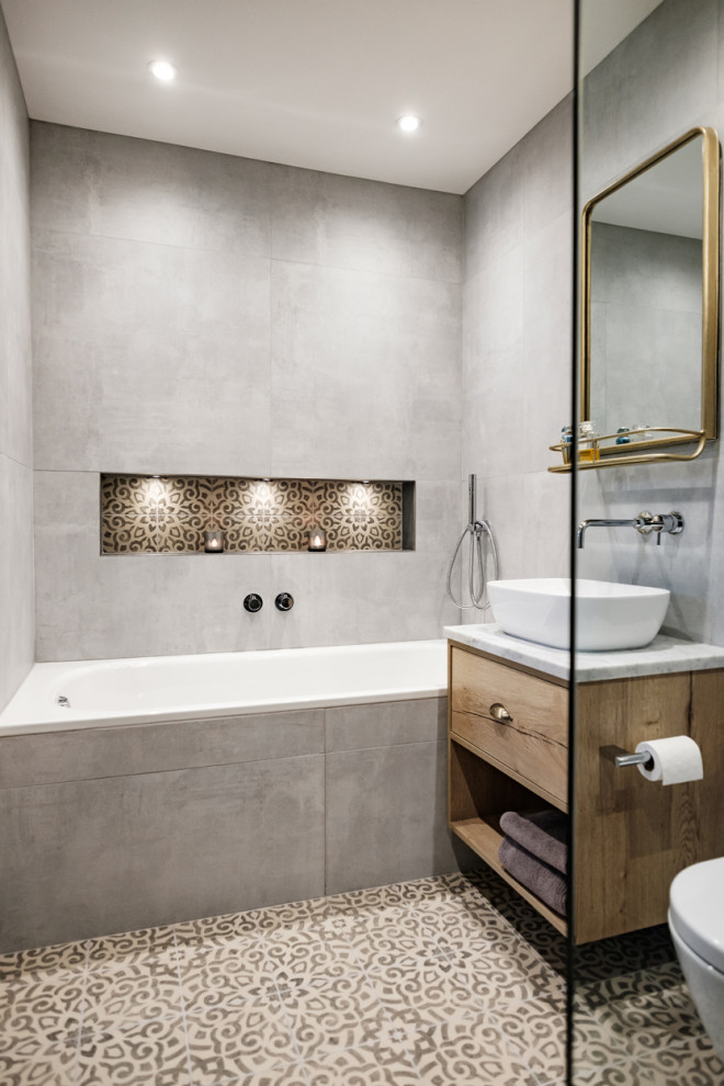 Modern inredning av ett mellanstort en-suite badrum, med skåp i mellenmörkt trä, en öppen dusch, en vägghängd toalettstol, grå kakel, ett fristående handfat, med dusch som är öppen, ett platsbyggt badkar, porslinskakel, klinkergolv i porslin och marmorbänkskiva