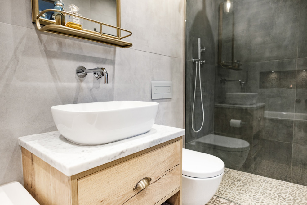 Inredning av ett industriellt mellanstort en-suite badrum, med skåp i mellenmörkt trä, ett platsbyggt badkar, en öppen dusch, en vägghängd toalettstol, grå kakel, porslinskakel, grå väggar, klinkergolv i porslin, ett fristående handfat, marmorbänkskiva och med dusch som är öppen