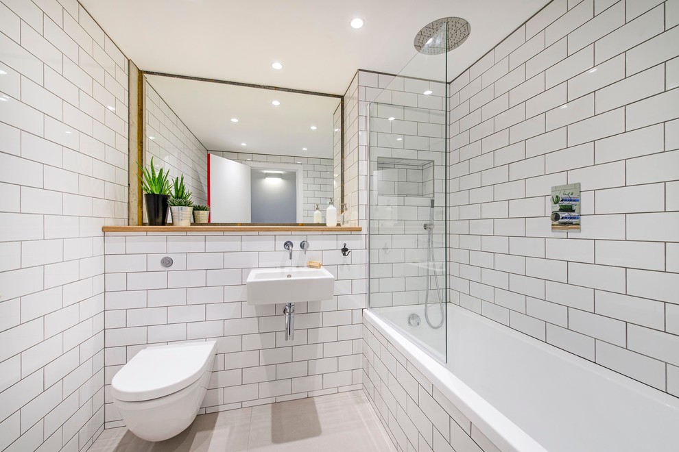 Industriell inredning av ett mellanstort badrum, med ett väggmonterat handfat, ett badkar i en alkov, en dusch/badkar-kombination, en vägghängd toalettstol, vit kakel och tunnelbanekakel