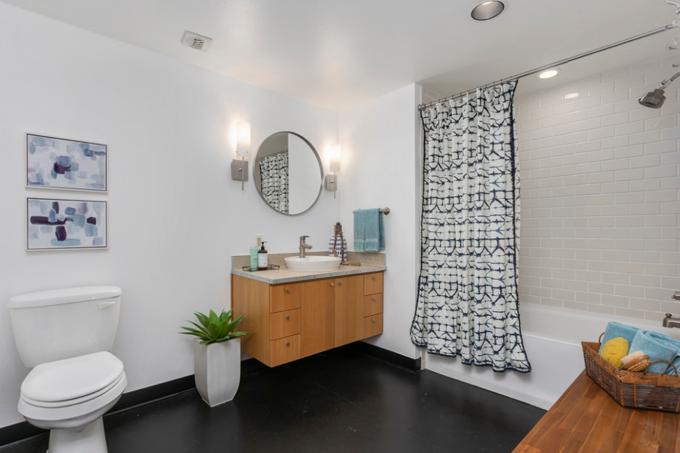 シアトルにある広いインダストリアルスタイルのおしゃれなマスターバスルーム (アルコーブ型浴槽、シャワー付き浴槽	、白いタイル、セラミックタイル、白い壁、クッションフロア、ベッセル式洗面器、黒い床、シャワーカーテン、ベージュのカウンター、洗面台1つ) の写真