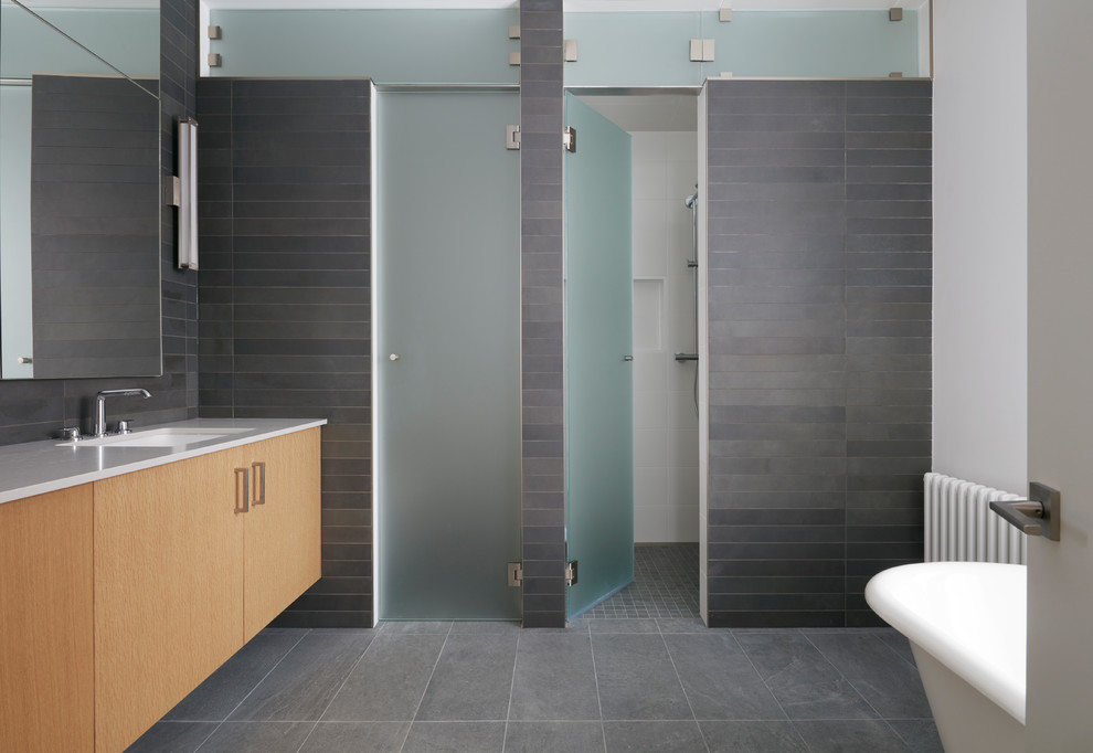 Стильный дизайн: большая главная ванная комната в стиле модернизм с плоскими фасадами, светлыми деревянными фасадами, ванной на ножках, душем в нише, унитазом-моноблоком, серой плиткой, керамической плиткой, белыми стенами, полом из керамогранита, врезной раковиной, столешницей из искусственного кварца, серым полом, душем с распашными дверями и белой столешницей - последний тренд