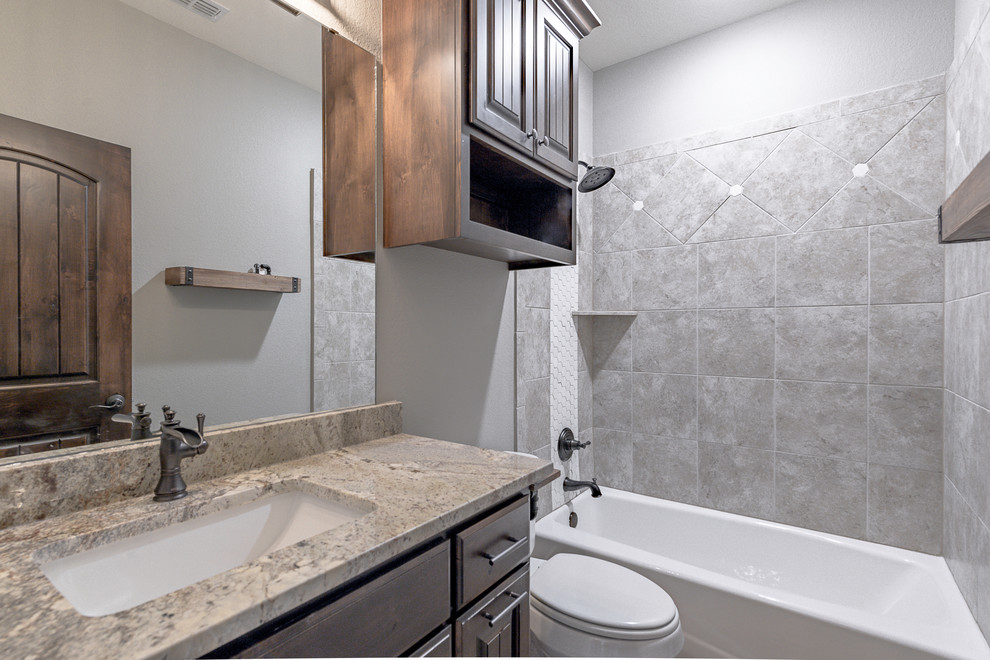Corner shower - mid-sized industrial kids' gray tile and ceramic tile ceramic tile and beige floor corner shower idea in Other with raised-panel cabinets, dark wood cabinets, a two-piece toilet, gray walls, an undermount sink, granite countertops and a hinged shower door