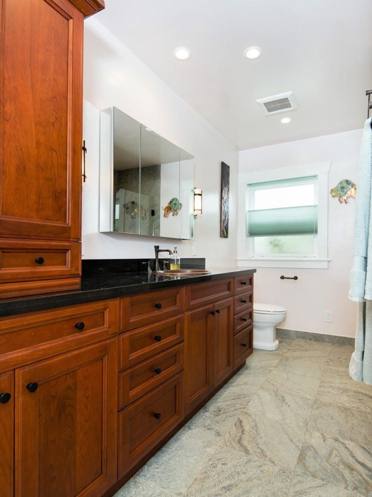 Inspiration for a mid-sized transitional master gray tile and stone tile gray floor and single-sink bathroom remodel in San Francisco with medium tone wood cabinets, beige walls, a drop-in sink, granite countertops, a hinged shower door and black countertops
