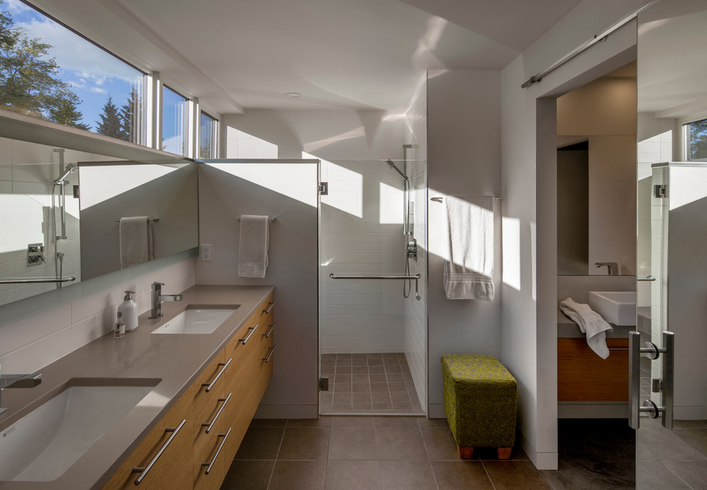 На фото: ванная комната в стиле модернизм с плоскими фасадами, светлыми деревянными фасадами, душем без бортиков, белой плиткой, плиткой кабанчик, белыми стенами, врезной раковиной, столешницей из искусственного камня, коричневым полом и душем с распашными дверями с