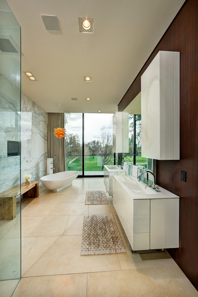 Inredning av ett modernt stort en-suite badrum, med släta luckor, vita skåp, ett fristående badkar, en kantlös dusch, vit kakel, ett integrerad handfat, bänkskiva i akrylsten, bruna väggar och kalkstensgolv