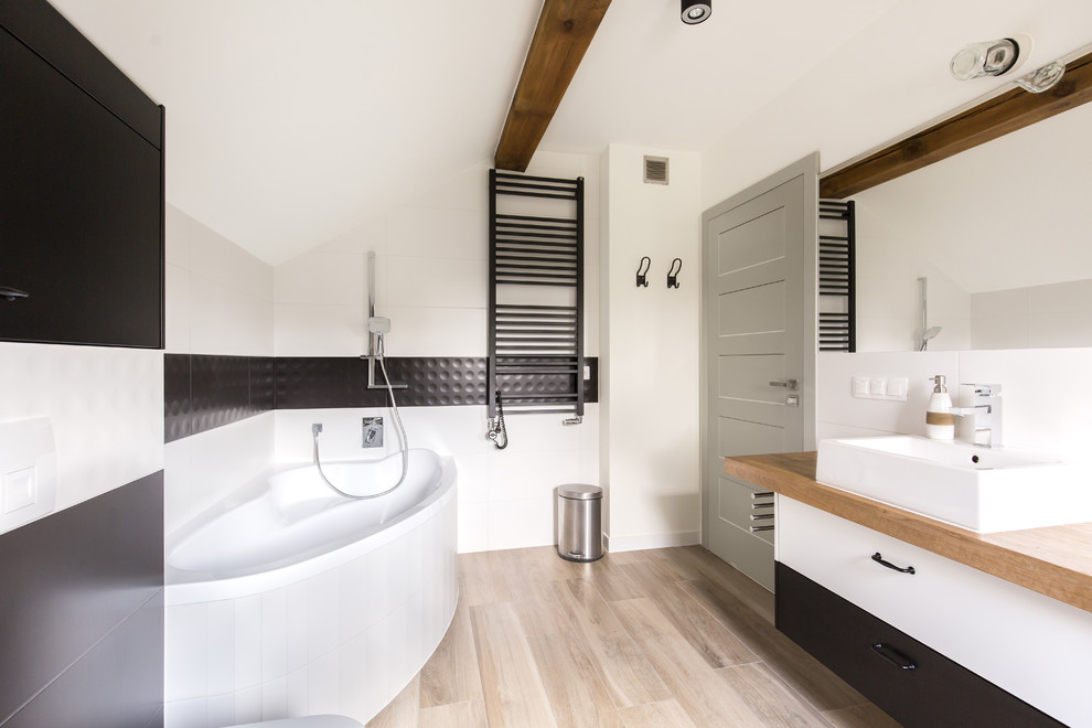 Idées déco pour une salle de bain principale contemporaine de taille moyenne avec un carrelage noir et blanc, un plan de toilette marron, un placard à porte plane, des portes de placard blanches, une baignoire d'angle, un mur blanc, une vasque, un plan de toilette en bois et un sol marron.