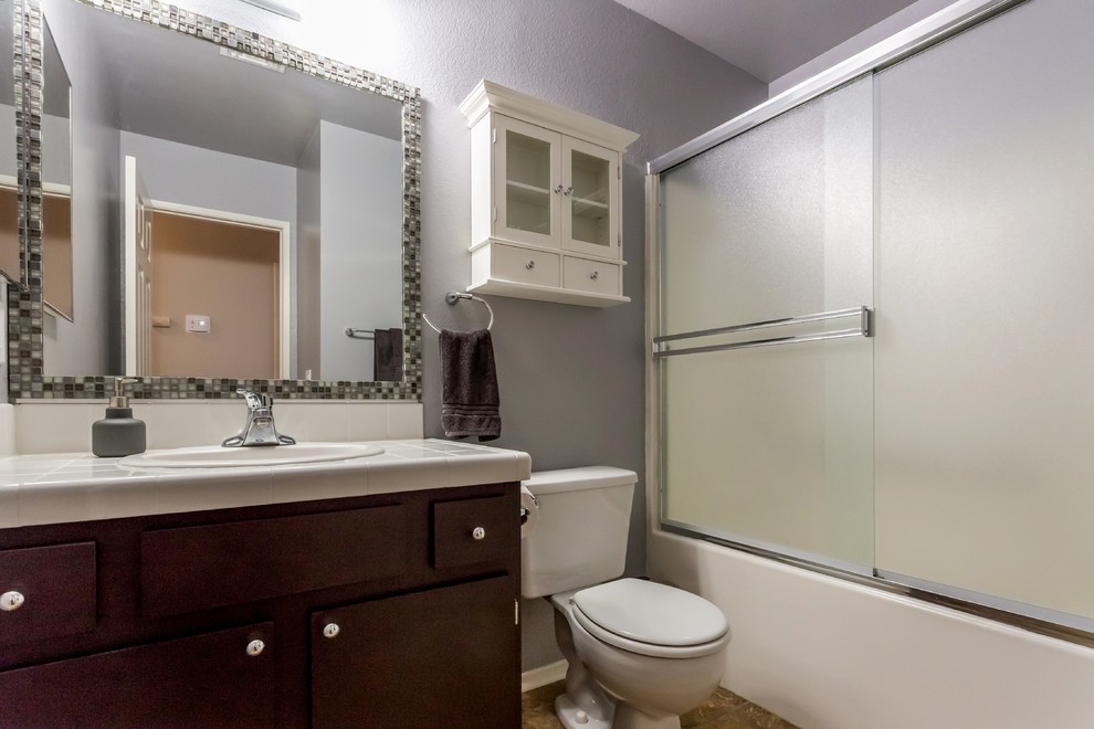 Exempel på ett litet eklektiskt vit vitt badrum för barn, med släta luckor, bruna skåp, ett badkar i en alkov, en dusch/badkar-kombination, en toalettstol med separat cisternkåpa, grå väggar, klinkergolv i keramik, ett nedsänkt handfat, kaklad bänkskiva, flerfärgat golv och dusch med skjutdörr