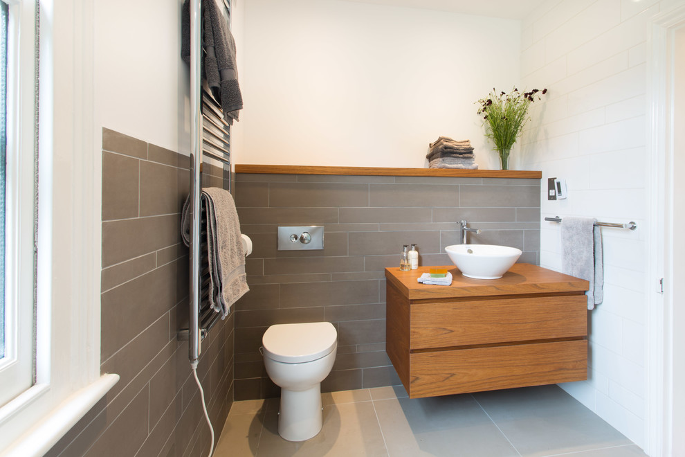 Cette image montre une petite salle de bain design en bois brun avec une vasque, un plan de toilette en bois, un carrelage gris, des carreaux de céramique, une douche ouverte, WC à poser et un sol en carrelage de céramique.