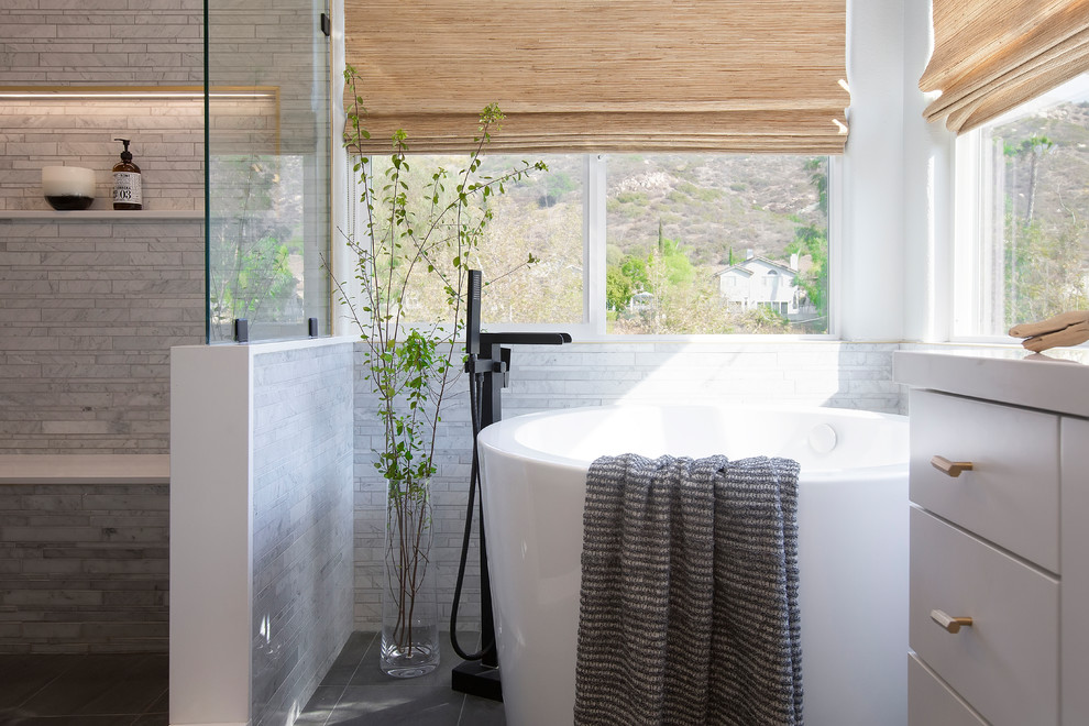 Photo of a contemporary bathroom in Phoenix with flat-panel cabinets, grey cabinets, a freestanding bath, a built-in shower, grey tiles, white walls, grey floors, an open shower and white worktops.