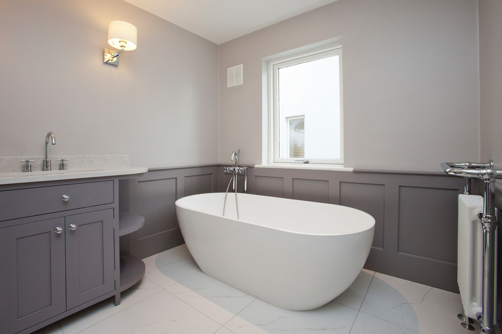 Medium sized traditional bathroom in Dublin with shaker cabinets, grey cabinets, a freestanding bath, a shower/bath combination, white tiles, grey walls, an integrated sink and white floors.