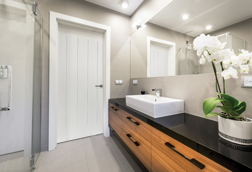 Exemple d'une salle de bain principale moderne en bois clair de taille moyenne avec un placard à porte plane, une douche ouverte, un carrelage gris, des carreaux de céramique, un mur gris, un sol en carrelage de céramique, une grande vasque et un plan de toilette en surface solide.