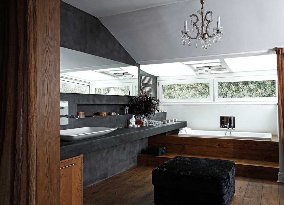 Modelo de cuarto de baño actual con lavabo sobreencimera, puertas de armario de madera en tonos medios, encimera de cemento, bañera encastrada y baldosas y/o azulejos grises