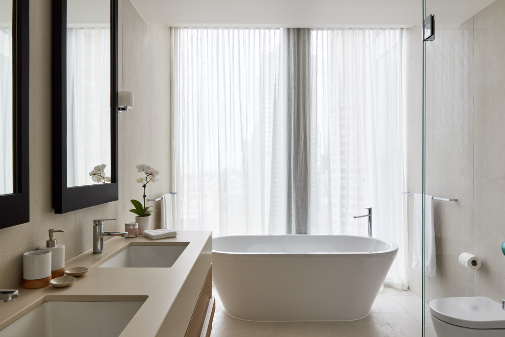 Example of a trendy master beige tile beige floor freestanding bathtub design in Melbourne with flat-panel cabinets, beige cabinets, a wall-mount toilet, beige walls, an undermount sink, a hinged shower door and beige countertops