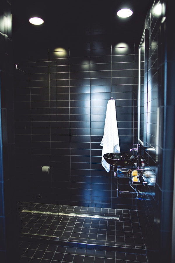 Foto de cuarto de baño infantil moderno pequeño con lavabo sobreencimera, encimera de vidrio, ducha abierta, sanitario de una pieza, baldosas y/o azulejos negros, suelo de baldosas de porcelana y baldosas y/o azulejos de cerámica