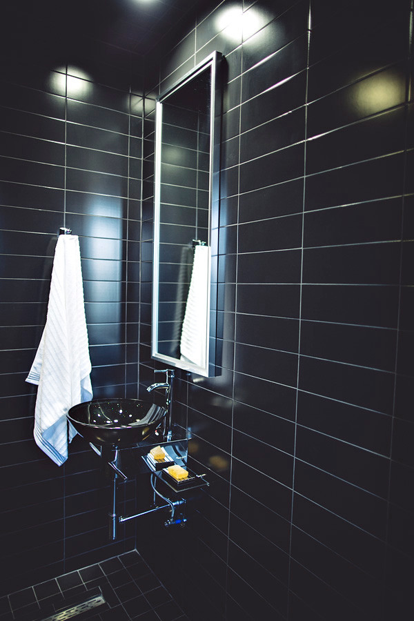 Esempio di una piccola stanza da bagno con doccia moderna con lavabo a bacinella, top in vetro, doccia aperta, WC monopezzo, piastrelle nere, piastrelle in ceramica e pavimento in gres porcellanato