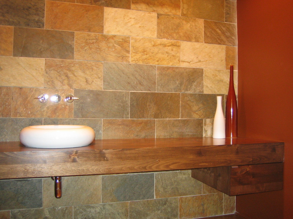 Diseño de cuarto de baño moderno con lavabo sobreencimera, armarios tipo mueble, puertas de armario de madera en tonos medios, encimera de madera, baldosas y/o azulejos grises y baldosas y/o azulejos de piedra