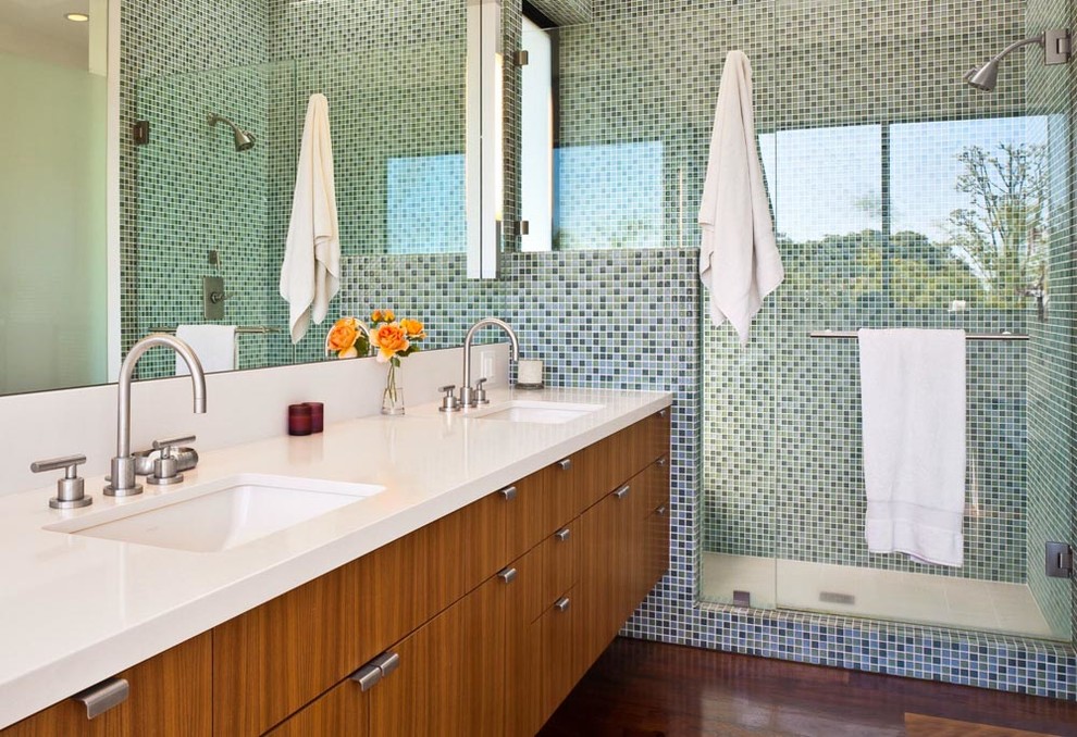 Modern inredning av ett badrum, med släta luckor, skåp i mellenmörkt trä, en dusch i en alkov, gröna väggar, mörkt trägolv och ett undermonterad handfat