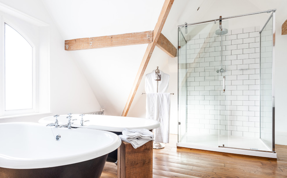 Inspiration pour une salle de bain nordique avec une baignoire sur pieds, un carrelage blanc, un carrelage métro, un mur blanc et un sol en bois brun.