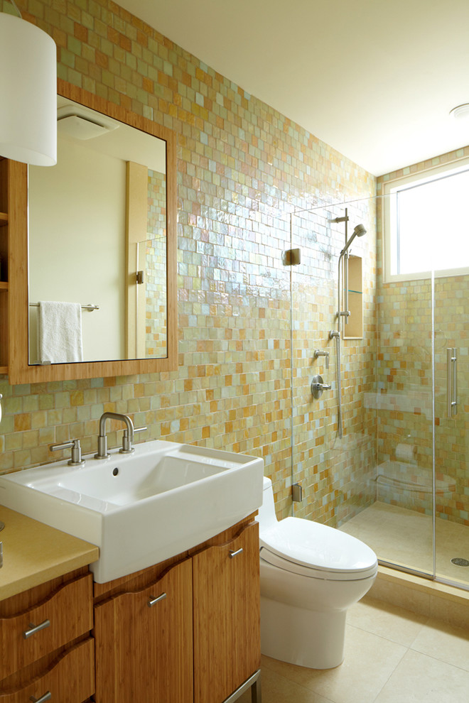 This is an example of a medium sized modern bathroom in New York with an integrated sink, flat-panel cabinets, medium wood cabinets, an alcove shower, a two-piece toilet, multi-coloured tiles, ceramic flooring and solid surface worktops.