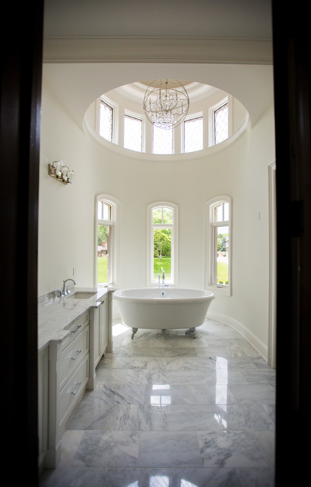 Пример оригинального дизайна: большая главная ванная комната в классическом стиле с фасадами с утопленной филенкой, белыми фасадами, ванной на ножках, белыми стенами, мраморным полом, врезной раковиной и мраморной столешницей