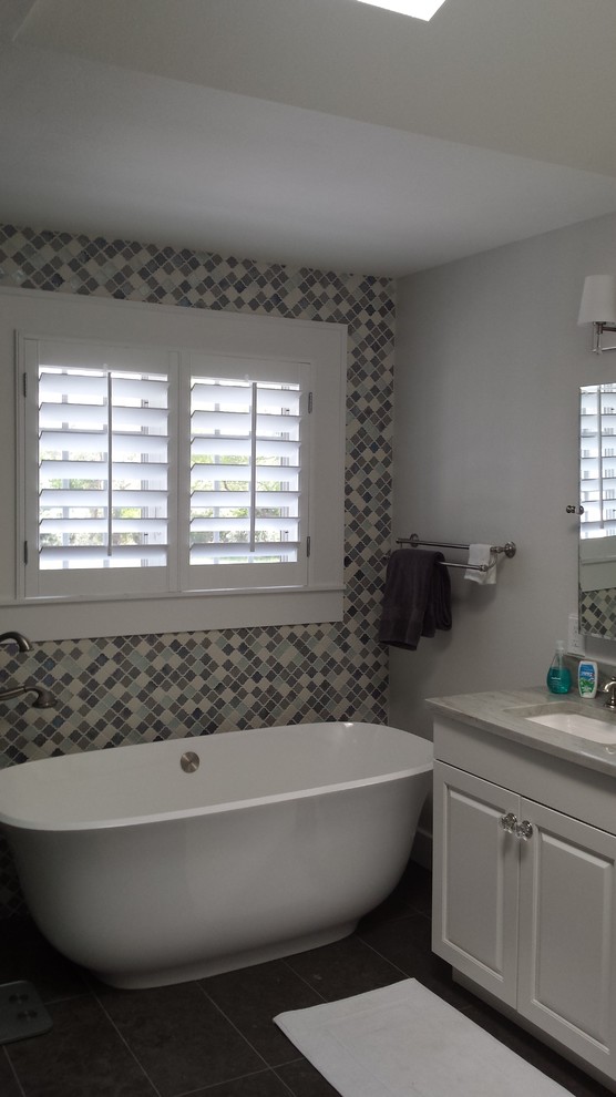 Стильный дизайн: главная ванная комната среднего размера в стиле модернизм с фасадами с выступающей филенкой, белыми фасадами, отдельно стоящей ванной, угловым душем, бежевой плиткой, черной плиткой, серой плиткой, разноцветной плиткой, розовой плиткой, белой плиткой, желтой плиткой, плиткой мозаикой, серыми стенами, полом из керамической плитки, врезной раковиной и столешницей из искусственного камня - последний тренд
