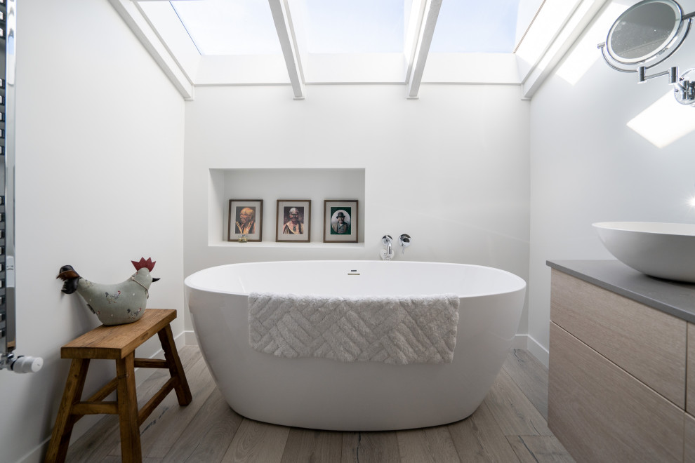 Cette image montre une salle de bain principale et beige et blanche design de taille moyenne avec un placard à porte plane, des portes de placard beiges, une baignoire indépendante, un mur blanc, une vasque, un sol beige, un plan de toilette gris, une niche et meuble-lavabo suspendu.