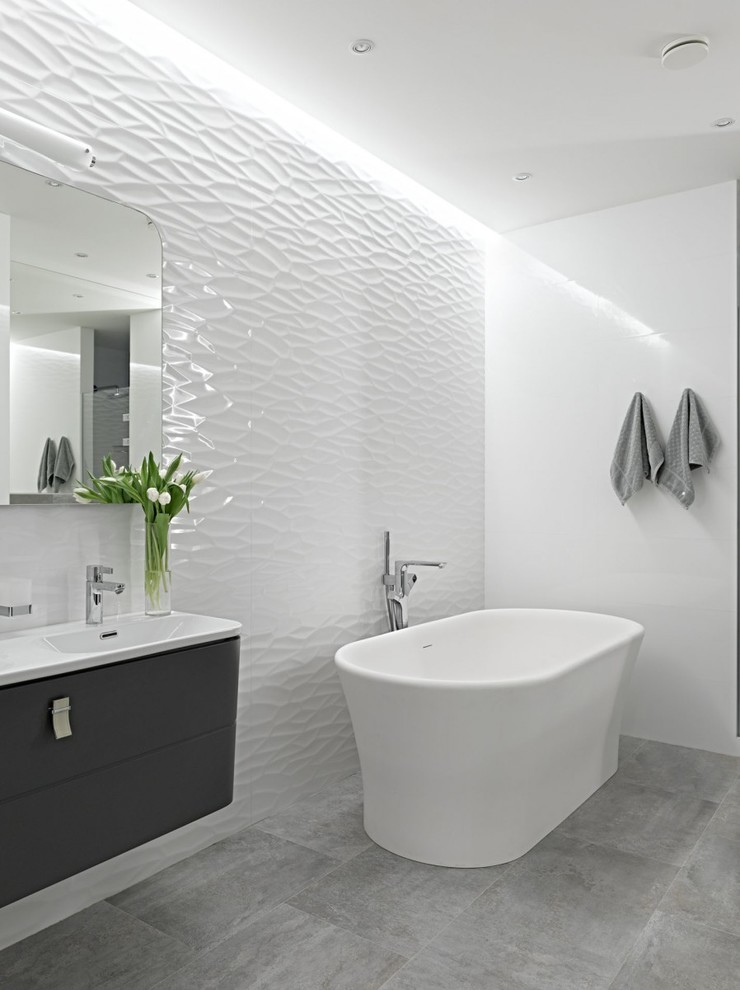 Modelo de cuarto de baño principal actual con armarios con paneles lisos, puertas de armario negras, bañera exenta, paredes blancas y lavabo integrado