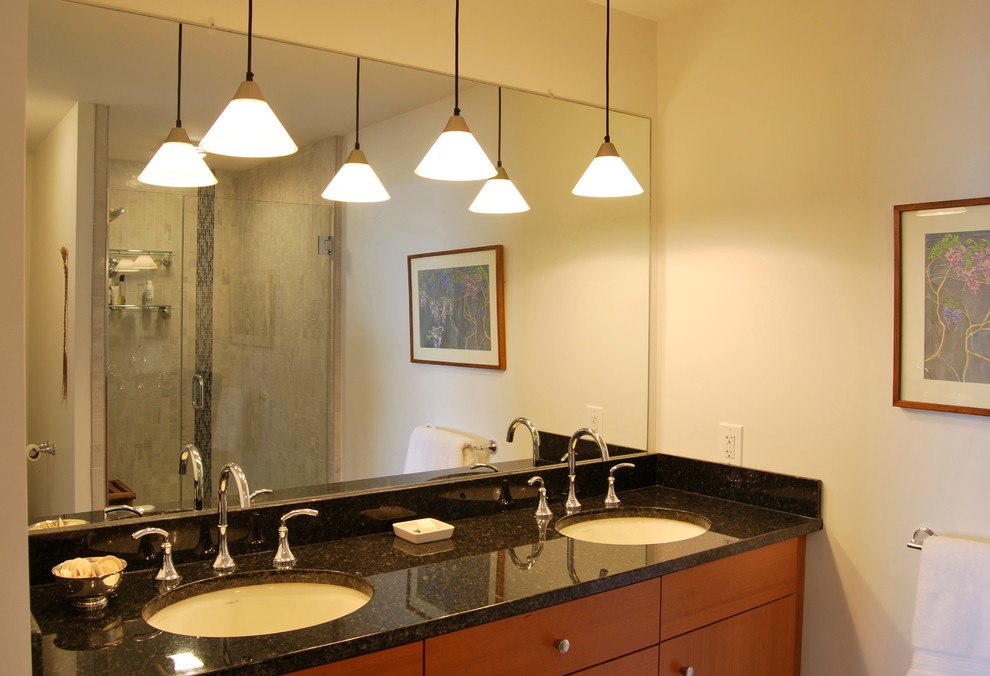 Diseño de cuarto de baño actual con lavabo bajoencimera, armarios con paneles lisos, puertas de armario de madera oscura, paredes blancas, encimera de granito, ducha empotrada y baldosas y/o azulejos grises
