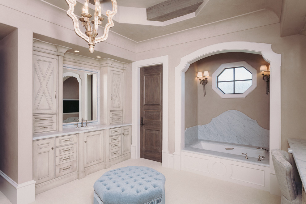 Immagine di una stanza da bagno padronale mediterranea con ante con riquadro incassato, ante beige, vasca sottopiano, piastrelle bianche, lastra di pietra, pareti beige, lavabo sottopiano, pavimento beige e top bianco