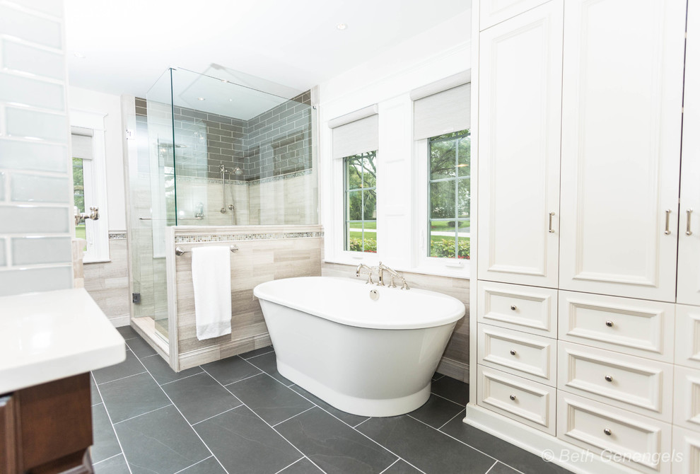 Large farmhouse ensuite bathroom in Chicago with flat-panel cabinets, dark wood cabinets, a freestanding bath, a corner shower, a one-piece toilet, beige tiles, limestone tiles, grey walls, ceramic flooring, a submerged sink, engineered stone worktops, grey floors, a hinged door and white worktops.