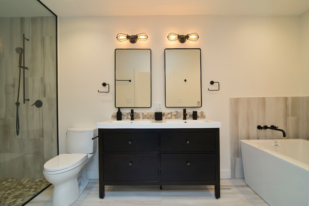 Photo of a medium sized industrial ensuite bathroom in Raleigh with flat-panel cabinets, black cabinets, a freestanding bath, a built-in shower, a two-piece toilet, multi-coloured tiles, porcelain tiles, white walls, porcelain flooring, an integrated sink, solid surface worktops, multi-coloured floors, an open shower and white worktops.