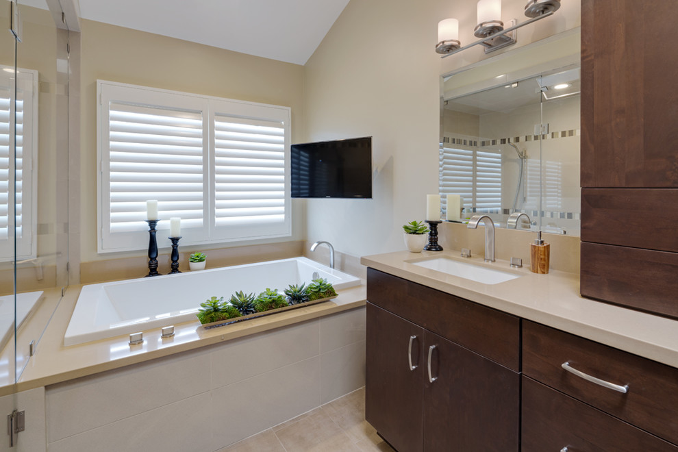 This is an example of a large classic ensuite bathroom in Orange County with a submerged sink, flat-panel cabinets, dark wood cabinets, solid surface worktops, a built-in bath, beige tiles, beige walls, ceramic flooring, a corner shower, beige floors and a hinged door.