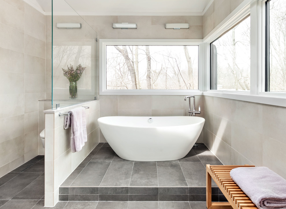 Photo of a large contemporary ensuite bathroom in New York with flat-panel cabinets, light wood cabinets, a freestanding bath, ceramic flooring, a corner shower, beige tiles, grey tiles, ceramic tiles, grey walls, a submerged sink, grey floors, a hinged door and grey worktops.