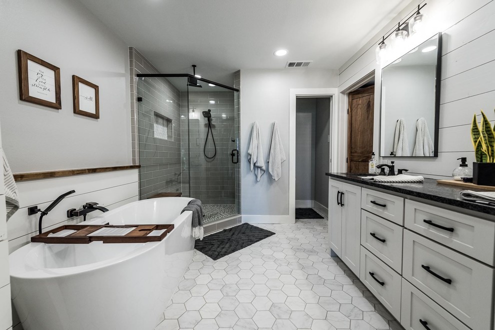 Пример оригинального дизайна: большая главная ванная комната в стиле кантри с фасадами в стиле шейкер, белыми фасадами, отдельно стоящей ванной, угловым душем, унитазом-моноблоком, серой плиткой, керамической плиткой, серыми стенами, полом из керамической плитки, врезной раковиной, столешницей из гранита, серым полом, душем с распашными дверями и черной столешницей